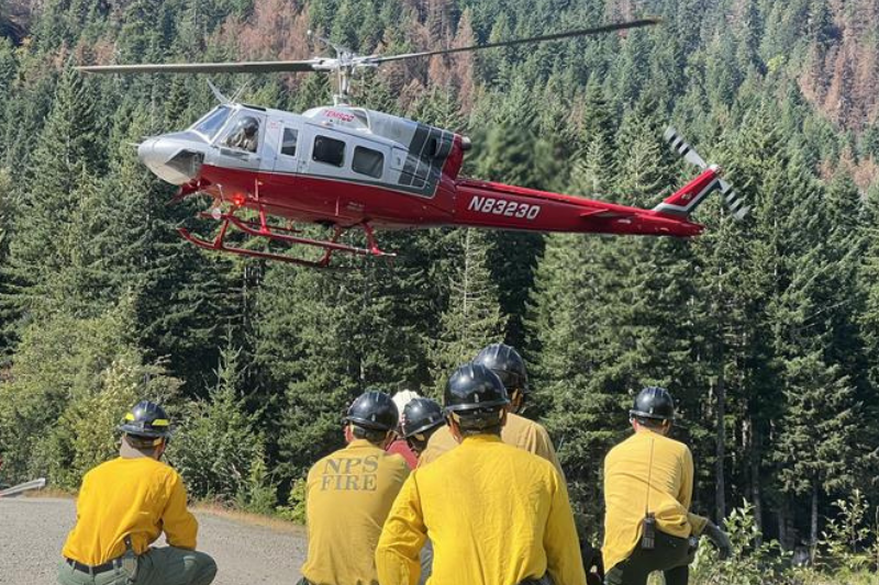 caption: On Aug. 24, 2025, firefighters working on the Bear Gulch wildfire in the Olympic National Forest wait for a helicopter shuttle. 