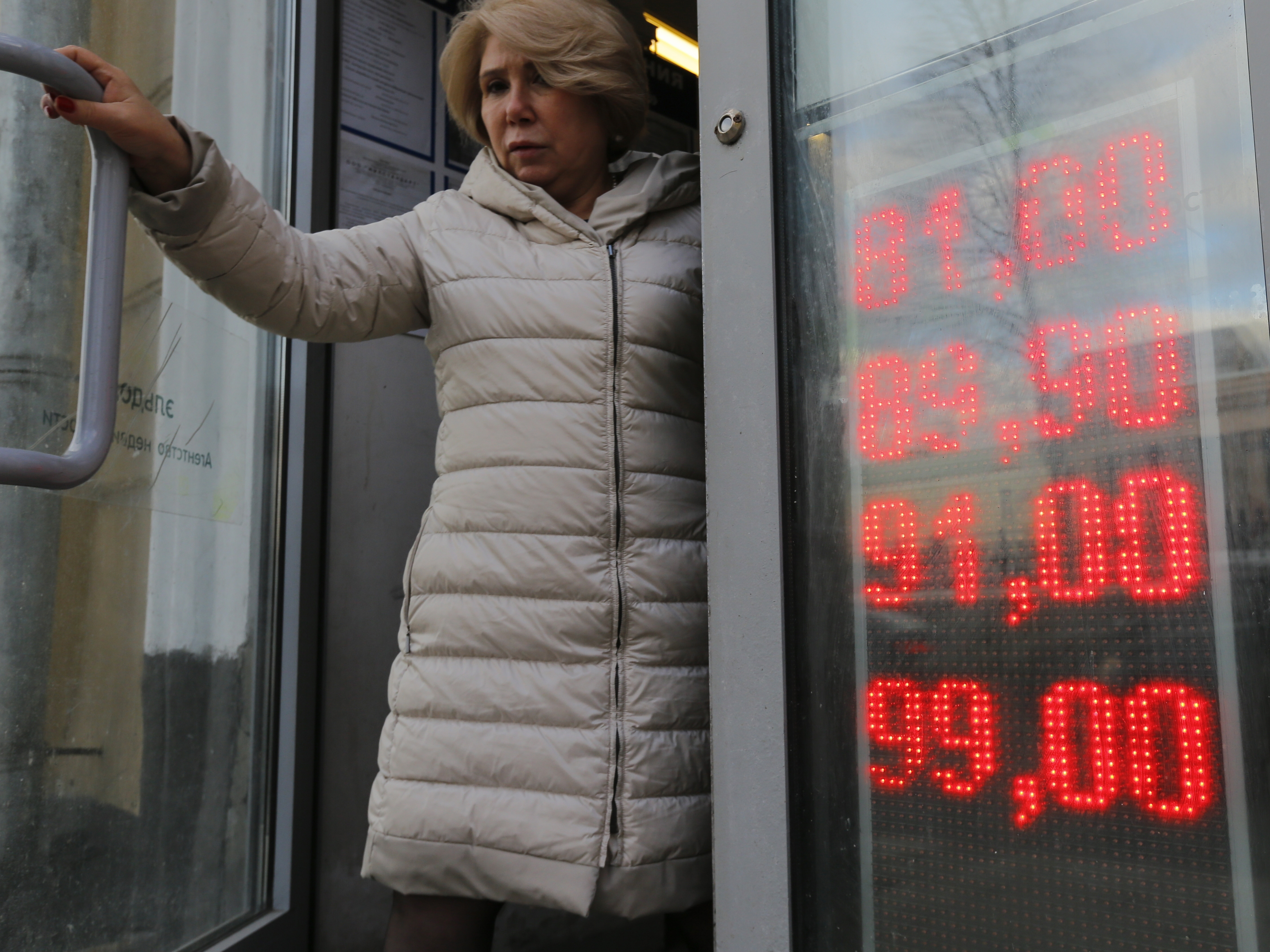 caption: A woman leaves a Moscow exchange office with a screen showing the currency exchange rates of the U.S. dollar and the euro to Russian rubles on Feb. 24.