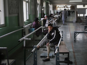 caption: Abdullah, 13, lost his left leg when he stepped on an improvised explosive device. He takes a break from walking practice at the International Committee of the Red Cross physical rehabilitation center in Kabul on Dec. 1, 2019.