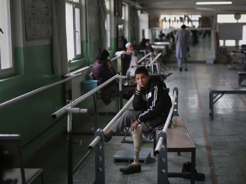 caption: Abdullah, 13, lost his left leg when he stepped on an improvised explosive device. He takes a break from walking practice at the International Committee of the Red Cross physical rehabilitation center in Kabul on Dec. 1, 2019.