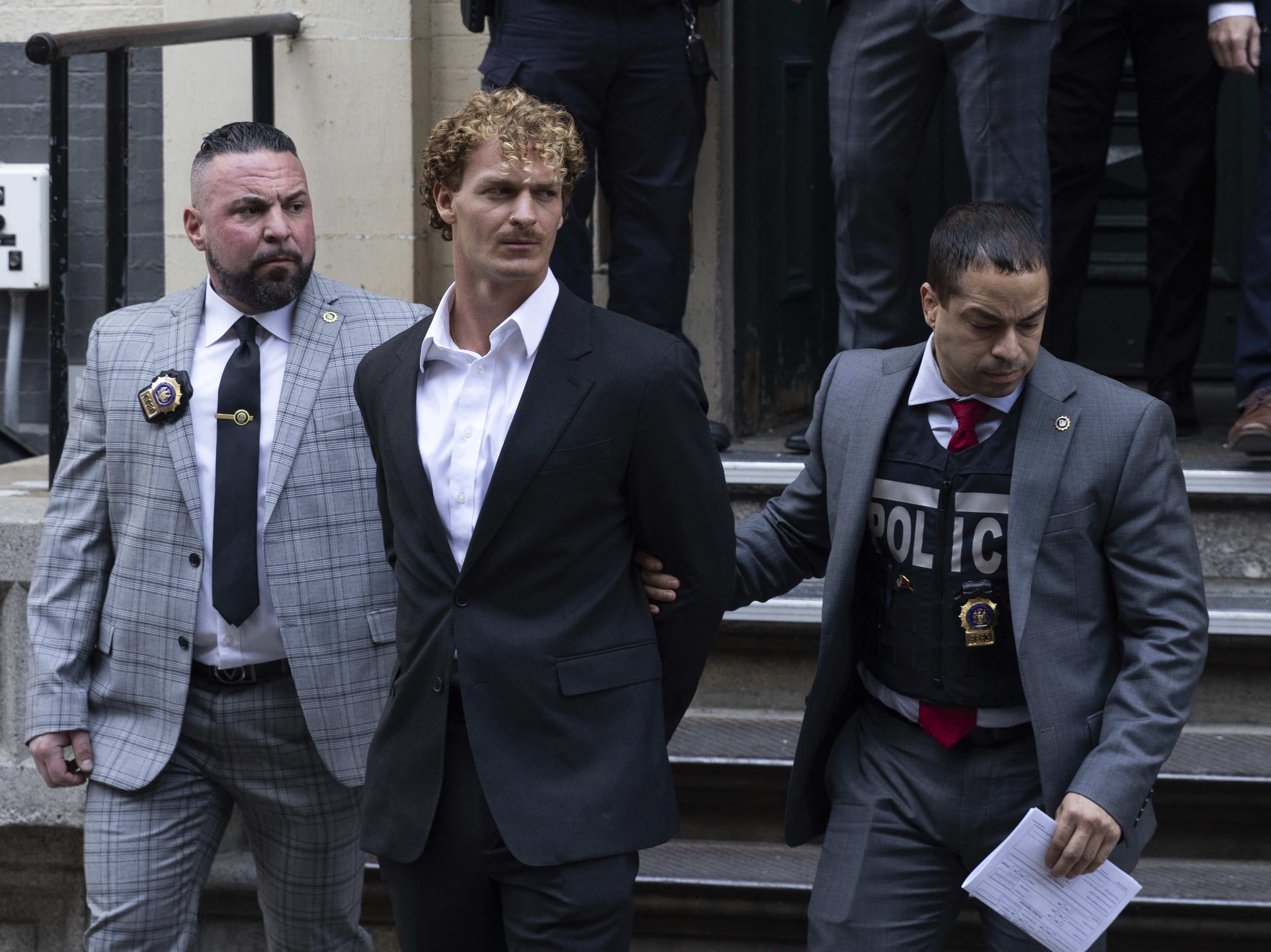 caption: Daniel Penny, center, is escorted by police after turning himself in for manslaughter charges in the death of Jordan Neely.