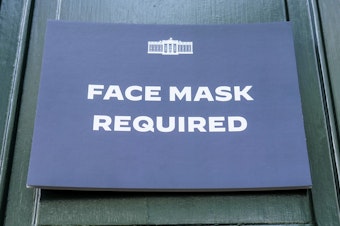 caption: A sign requiring the wearing of face masks is displayed at the testing center for visitors to the White House on July 30, 2022 in Washington, DC.