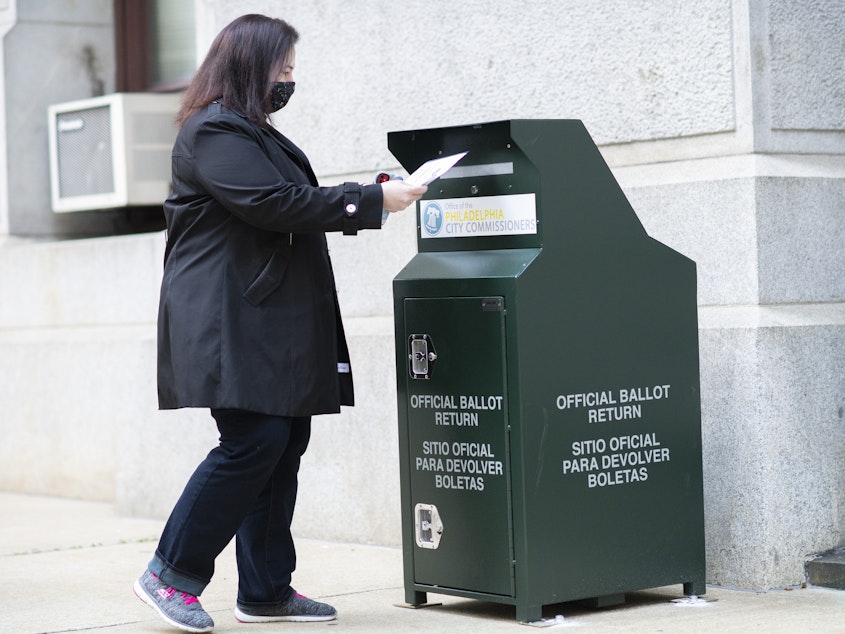 caption: A voter casts her early voting ballot at drop box outside of City Hall on Oct. 17, 2020 in Philadelphia.