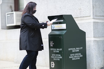 caption: A voter casts her early voting ballot at drop box outside of City Hall on Oct. 17, 2020 in Philadelphia.