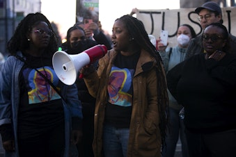 caption: Jaleesa Trapp, center, speaks to a crowd gathered at the intersection of 11th Street and Martin Luther King Jr. Way after a jury found three Tacoma police officers not guilty in the trial over the death of 33-year-old Manuel Ellis, on Thursday, December 21, 2023, in Tacoma. 