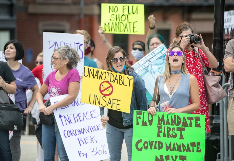 caption: Anti-vaccine activists protested at the Massachusetts State House in August against Governor Charlie Baker's mandate that all students enrolled in child care, pre-school, K-12, and post-secondary institutions must receive the flu vaccine this year.