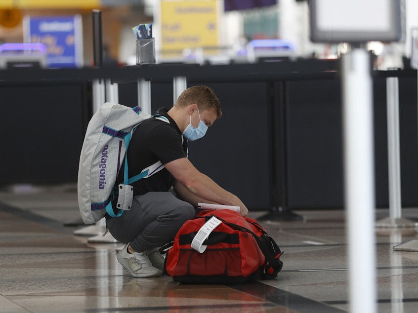 caption: A passenger wears a face covering at Denver International Airport as he checks his bags.