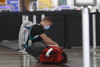 caption: A passenger wears a face covering at Denver International Airport as he checks his bags.