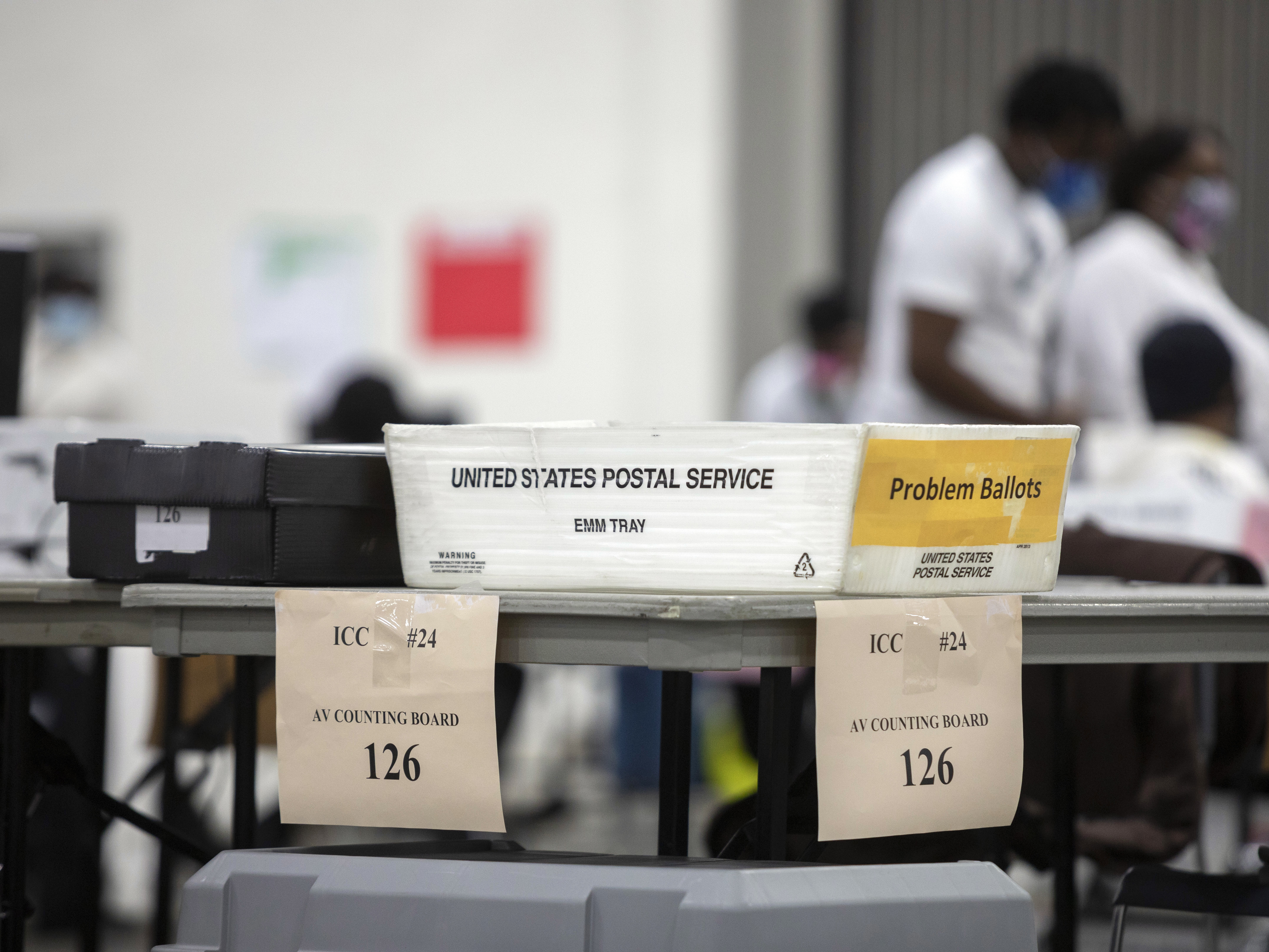 caption: A problem ballot box is placed on the end of a table where workers with the Detroit Department of Elections sorts through absentee ballots.