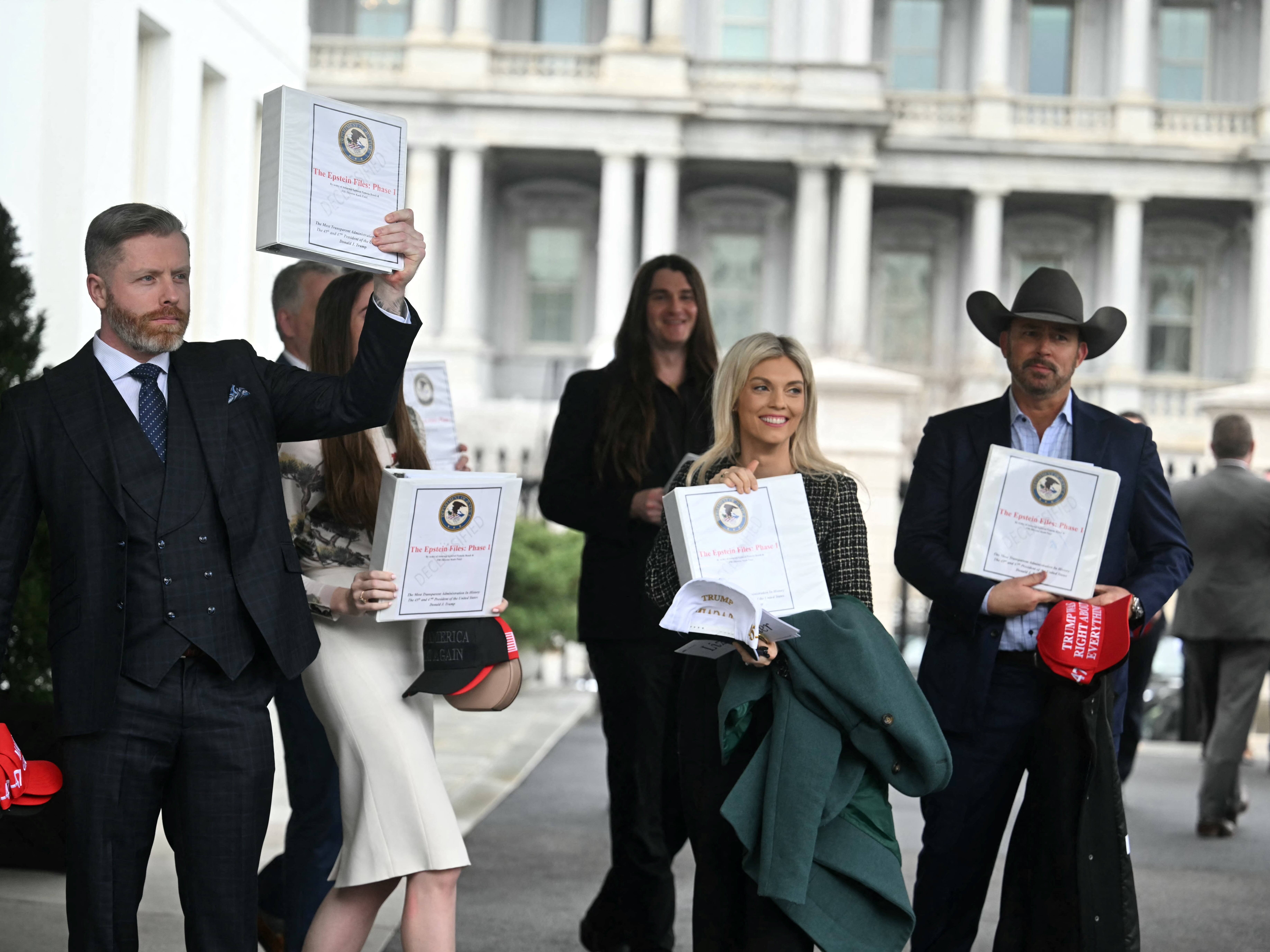 caption: (From L) Political commentator Rogan O'Handley, aka DC Draino, TikToker Chaya Raichik, conservative activist Scott Presler, commentator Liz Wheeler and conservative political commentator Chad Prather carry binders containing Jeffrey Epstein files out of the White House on Thursday.
