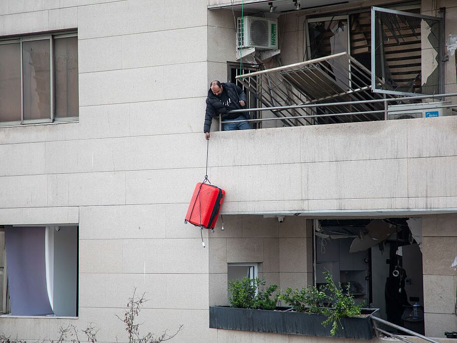 caption: A man lowers a suitcase from the balcony of a building damaged by a strike in a commercial district of Tehran, Iran, during the U.S.-Israeli war on Iran, Sunday.