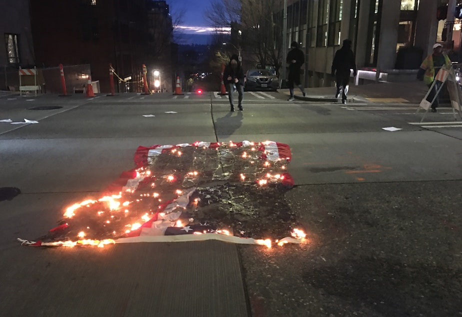 caption: An American flag burns in downtown Seattle on Inauguration Day, January 20, 2021. Protestors in black bloc say the change in leadership is symbolic and demand an end to U.S. Immigration and Customs Enforcement. 