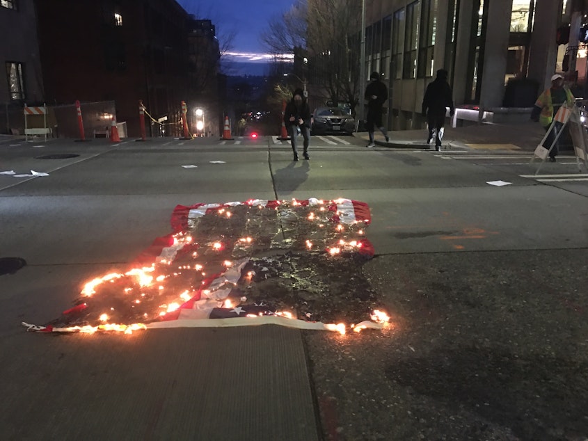 caption: An American flag burns in downtown Seattle on Inauguration Day, January 20, 2021. Protestors in black bloc say the change in leadership is symbolic and demand an end to U.S. Immigration and Customs Enforcement. 