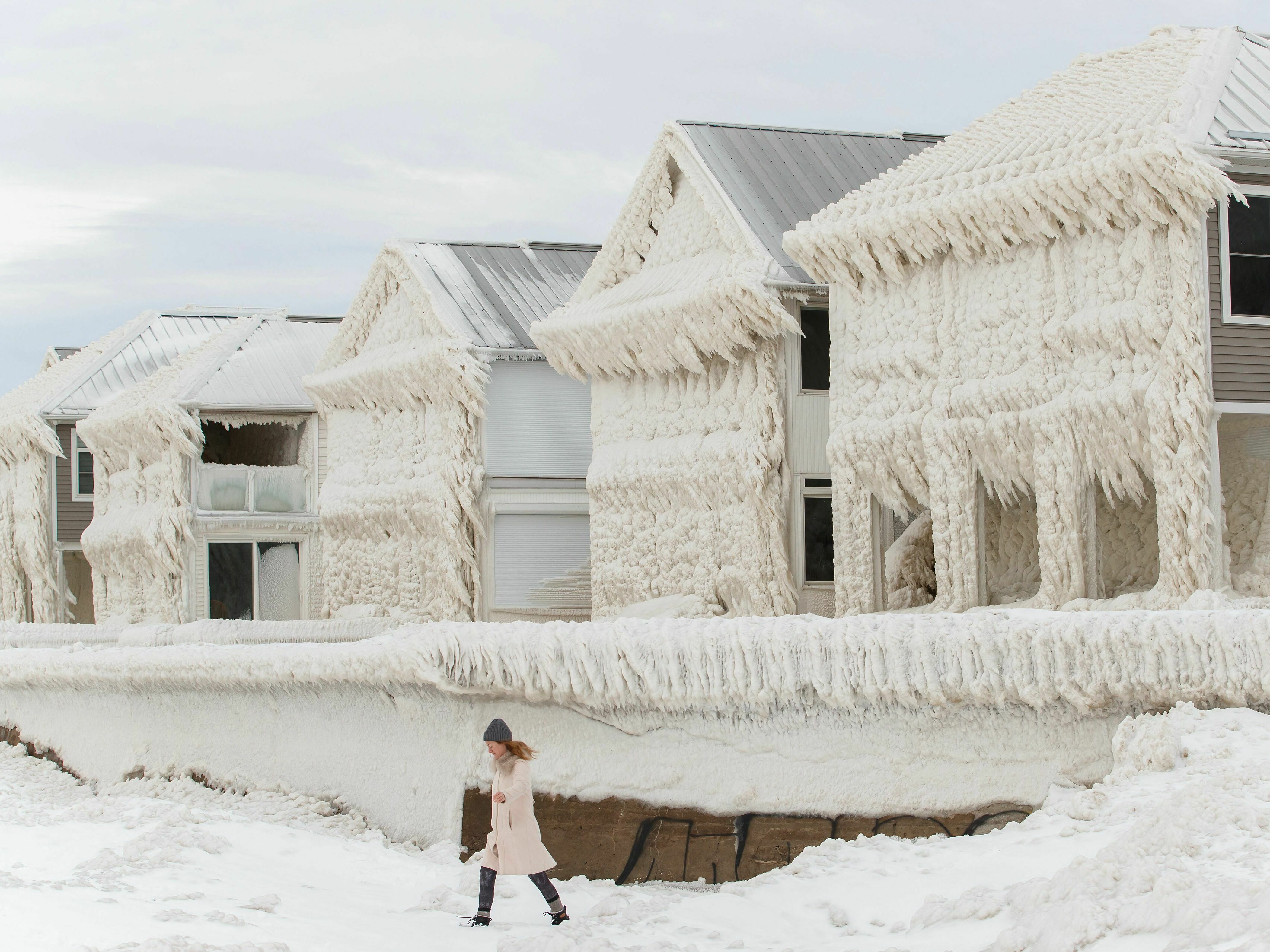 caption: A person walks by homes covered in ice at the waterfront community of Crystal Beach in Fort Erie, Ontario, Canada, on Wednesday, following a massive snowstorm that knocked out power in the area to thousands of residents.