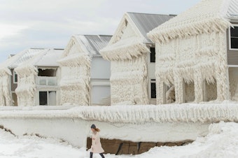 caption: A person walks by homes covered in ice at the waterfront community of Crystal Beach in Fort Erie, Ontario, Canada, on Wednesday, following a massive snowstorm that knocked out power in the area to thousands of residents.