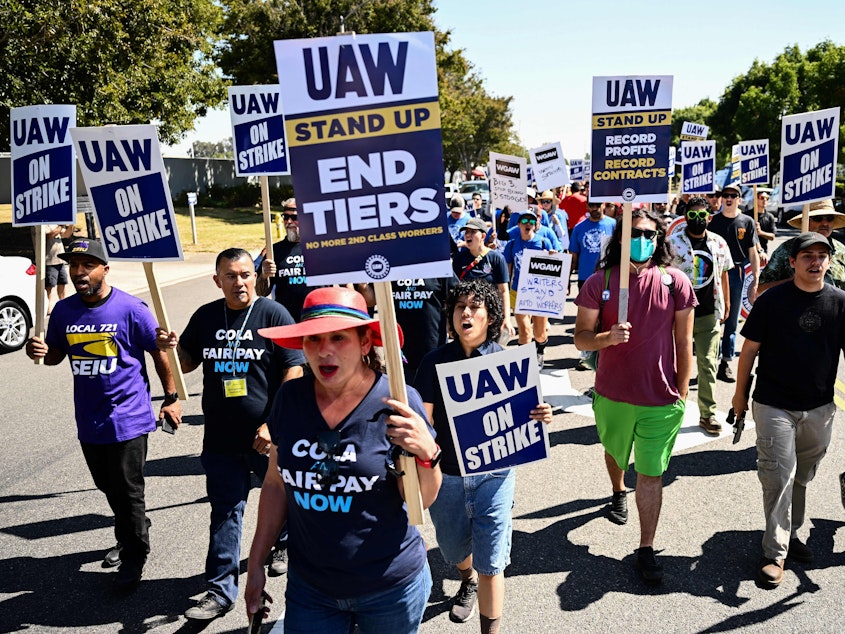 caption: Labor supporters and UAW members walk along a picket line during a strike outside of the Stellantis Chrysler Los Angeles Parts Distribution Center in Ontario, Calif., on Sept. 26, 2023.