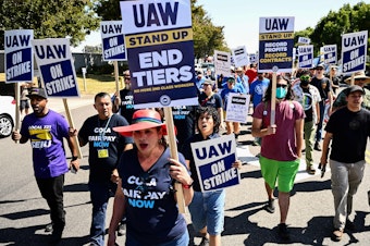 caption: Labor supporters and UAW members walk along a picket line during a strike outside of the Stellantis Chrysler Los Angeles Parts Distribution Center in Ontario, Calif., on Sept. 26, 2023.
