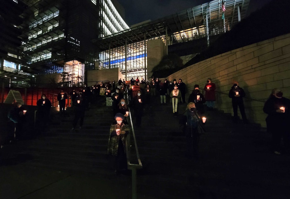 caption: Volunteers stand in silence for one hour on the steps of Seattle City Hall to honor those who died in 2021 on Tuesday, December 21, 2021.