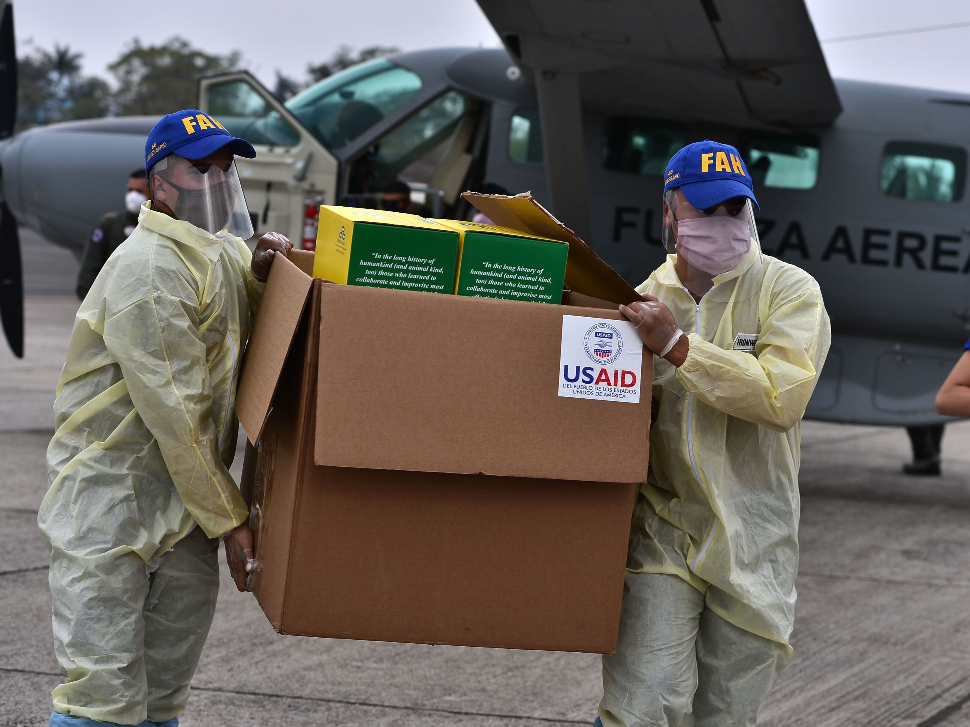 caption: After being inaugurated for his second president term, President Donald Trump has frozen virtually all U.S. foreign aid and issued a "stop work" order for groups in other countries that are funded by the U.S. government. Above: At the start of the pandemic, members of the Honduran Armed Forces carry a box containing diagnostic kits to test for COVID-19, donated by the United States Agency for International Development and the International Organization for Migration.