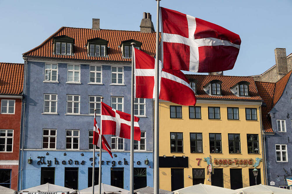 caption: COPENHAGEN, DENMARK - 2025/06/09: Danish flag seen fluttering in Nyhavn during the Royal Run. The Royal Run in Copenhagen is part of a nationwide annual event held across several cities in Denmark, first launched in 2018 to celebrate the 50th birthday of then-Crown Prince Frederik (now King Frederik X). Since then, it has become a cherished tradition promoting health, fitness, and community spirit among people of all ages and abilities. Marketed as the world's largest royal amateur sporting event, the Royal