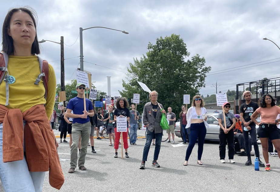 caption: Eliza Pan, a former Amazon employee, listens to speakers at a rally opposing the creation of an Amazon warehouse facility in Seattle's Mount Baker neighborhood on Saturday, July 23, 2022.