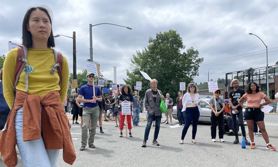 caption: Eliza Pan, a former Amazon employee, listens to speakers at a rally opposing the creation of an Amazon warehouse facility in Seattle's Mount Baker neighborhood on Saturday, July 23, 2022.