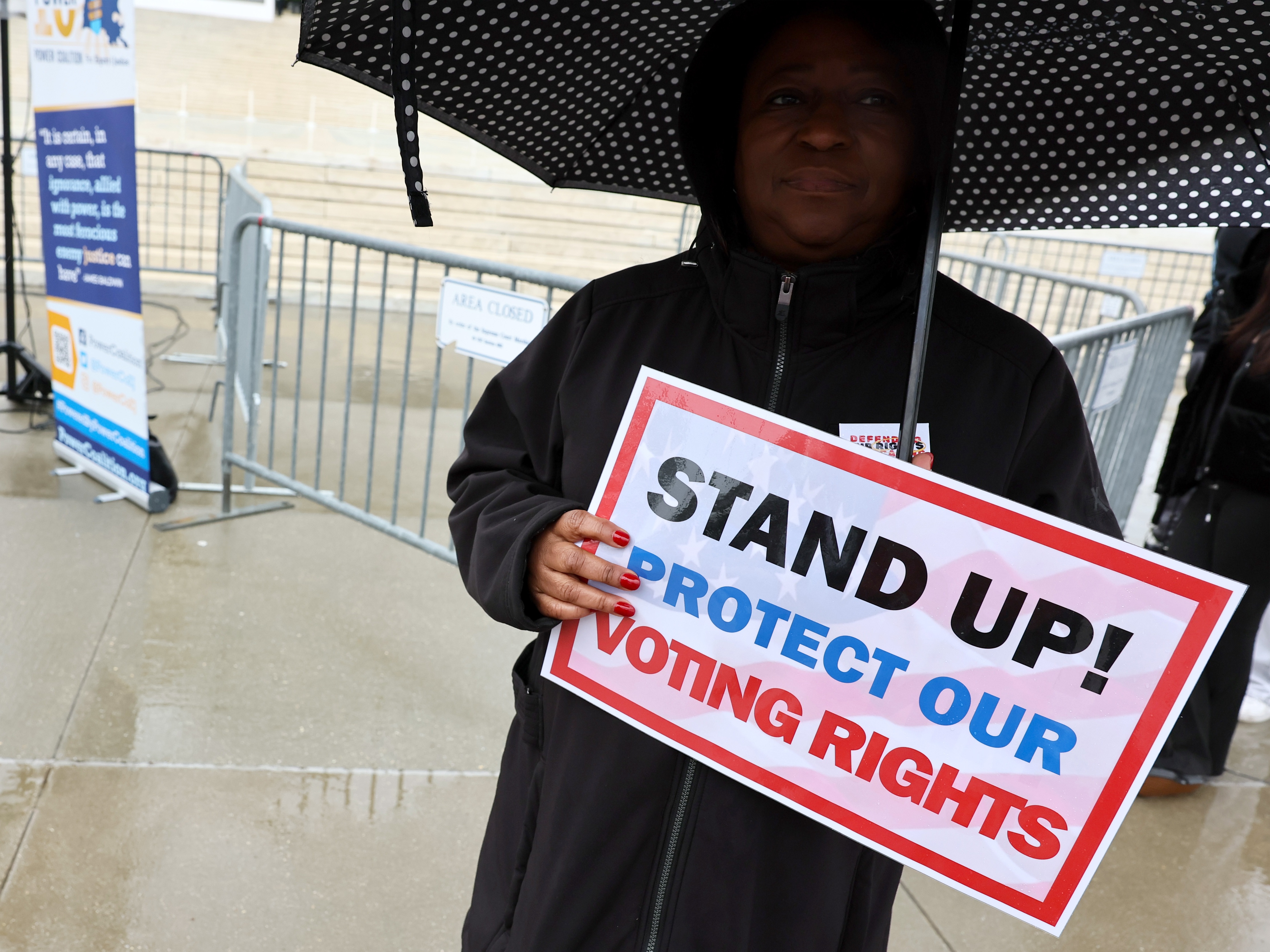 caption: A demonstrator holds an umbrella and a sign saying "STAND UP! PROTECT OUR VOTING RIGHTS" outside the U.S. Supreme Court in March in Washington, D.C.