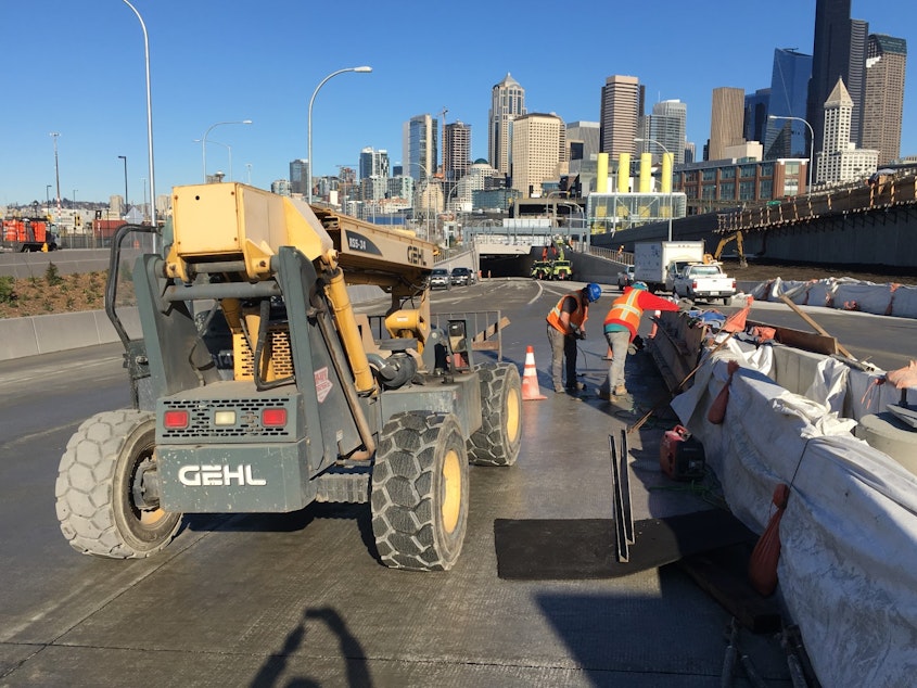 caption: Workers remove forms from curing concrete barriers, one of the final steps in the days before Seattle's new waterfront tunnel opens.