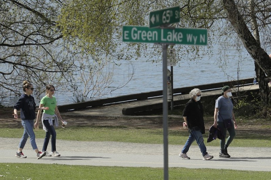 caption: Some people wearing masks, and some not, walk on a pathway at Green Lake Park, Friday, April 10, 2020, in Seattle.