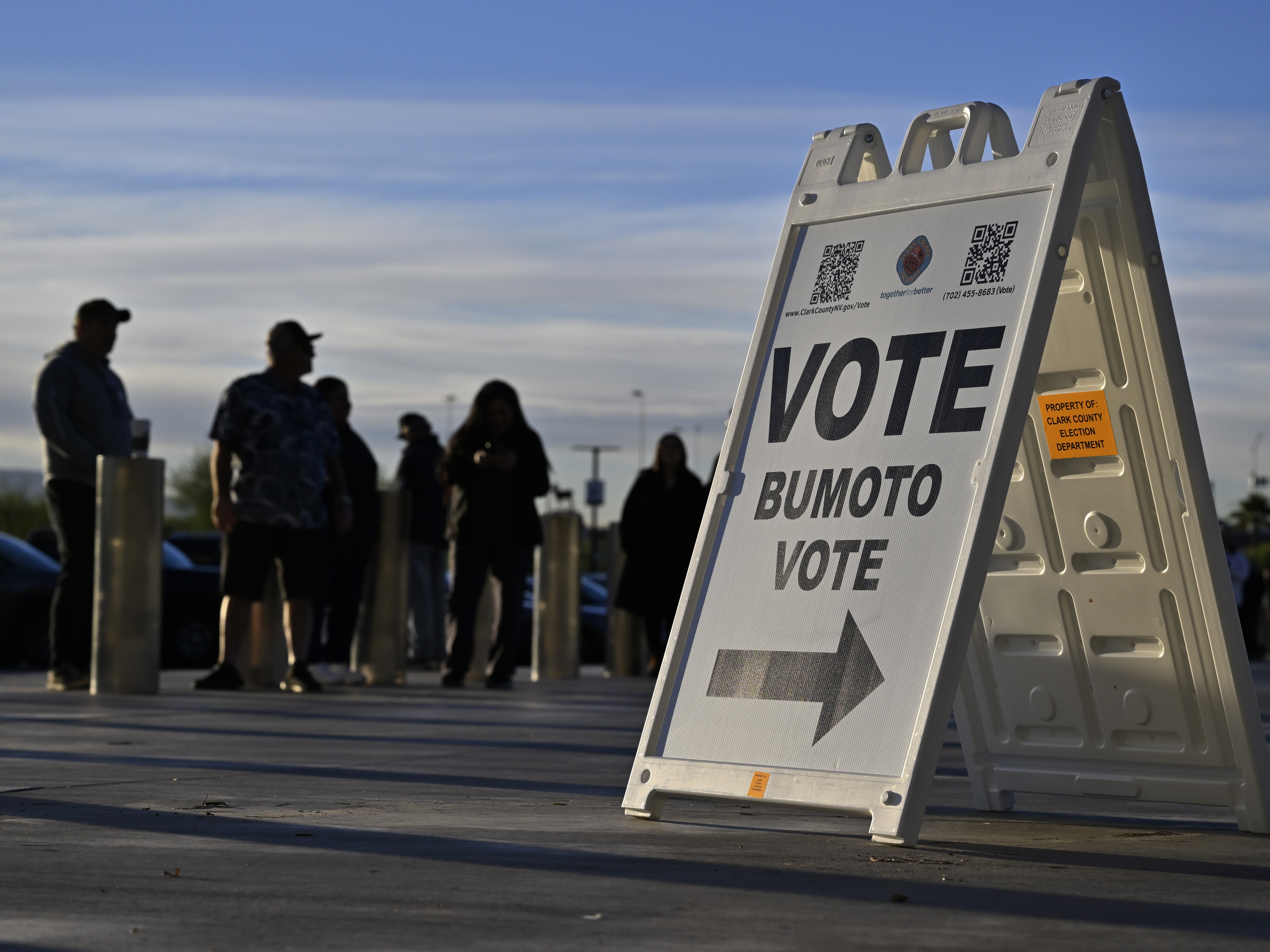 caption: Voters line up to cast their ballots at Allegiant Stadium on Nov. 5, 2024, in Las Vegas, behind a sign reading "Vote, Bumoto, Vote" — directions in English, Tagalog and Spanish.
