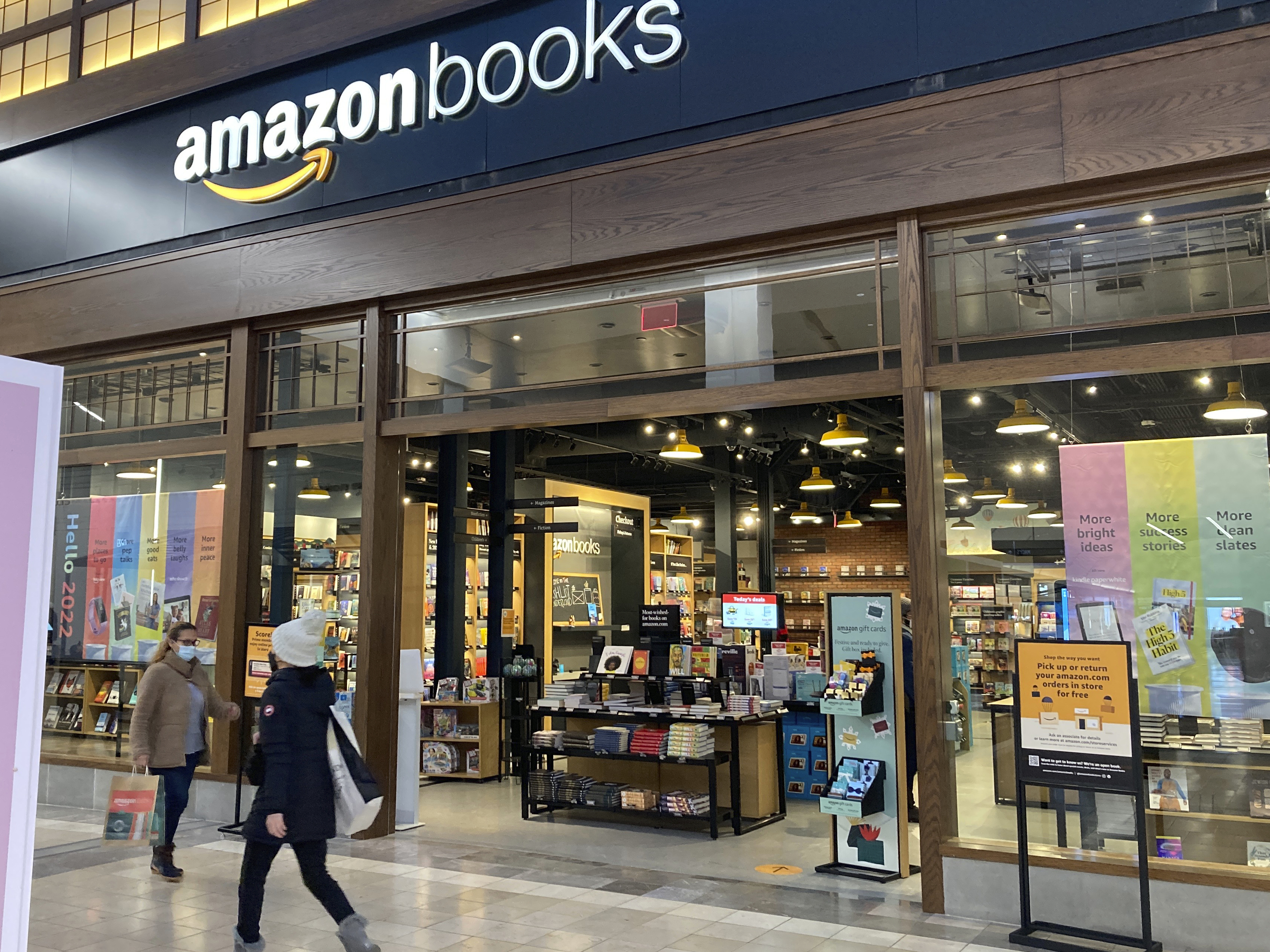 caption: People walk by an Amazon Books store at the Westfield Garden State Plaza shopping mall in Paramus, N.J., on Jan. 10, 2022.