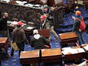 caption: Bruno Cua, 18, is allegedly seen here with his back to the camera, holding a tan jacket. Prosecutors say he entered the Senate Chamber of the U.S. Capitol on Jan. 6 with a handful of other rioters.