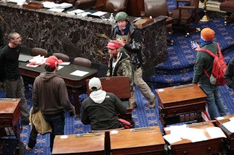 caption: Bruno Cua, 18, is allegedly seen here with his back to the camera, holding a tan jacket. Prosecutors say he entered the Senate Chamber of the U.S. Capitol on Jan. 6 with a handful of other rioters.