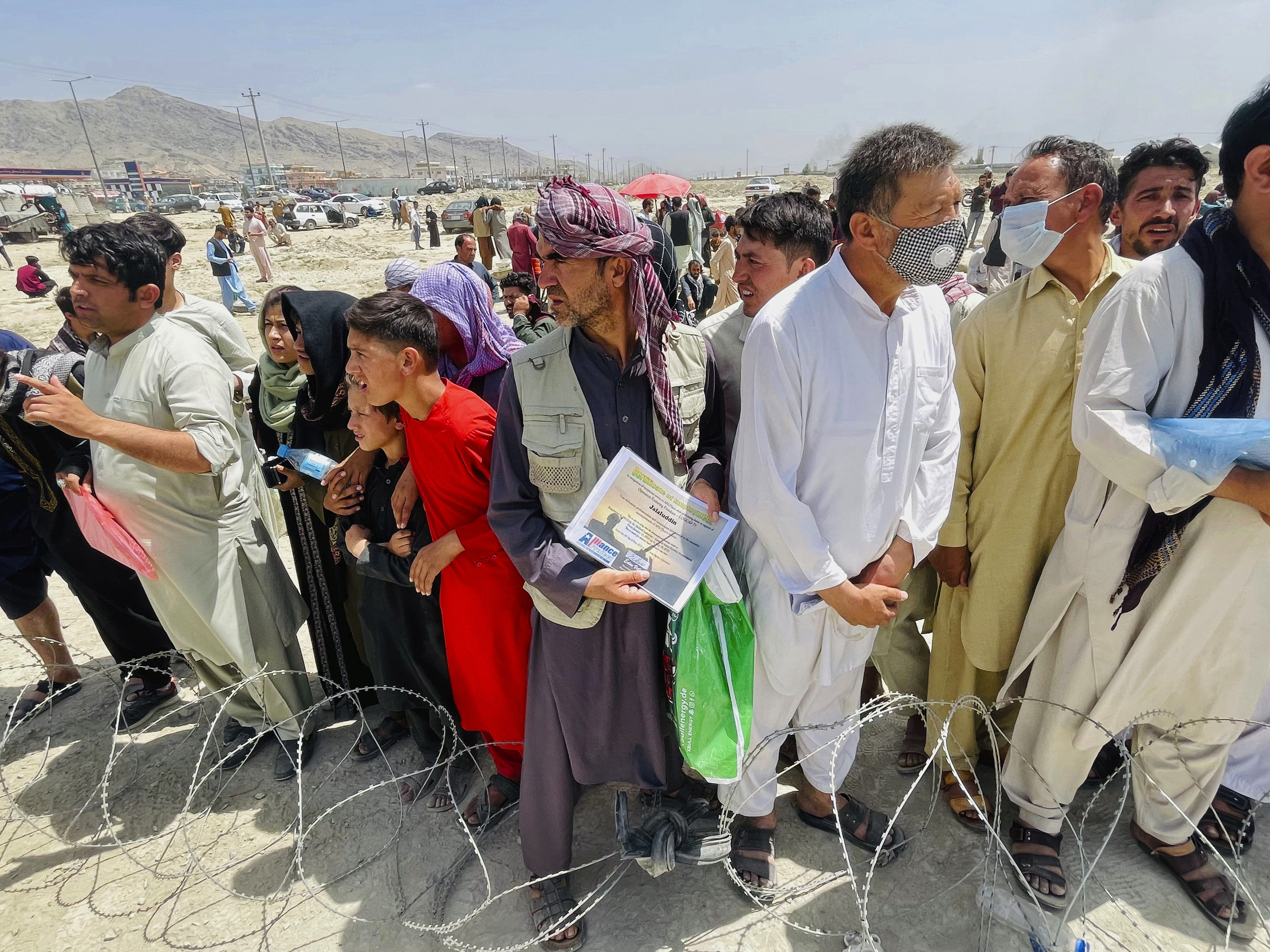caption: A man holds a certificate acknowledging his work for Americans as hundreds of people gather outside the international airport in Kabul, Afghanistan, Tuesday.