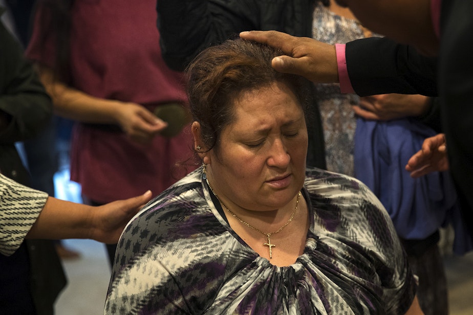 caption: Herainia Gonzalez is surrounded as people pray for her during a church service in the basement of Nathan Robert's home, on Sunday, September 16, 2018, in Des Moines.