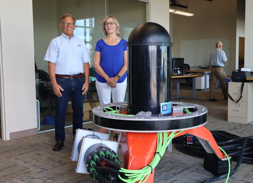 caption: Tim and Bev Acker, CEO and CFO respectively of Biosonics, stand beside the Seattle company’s new ocean-bottom sonar device, which is designed to facilitate marine energy permitting by identifying and tracking nearby sea life.