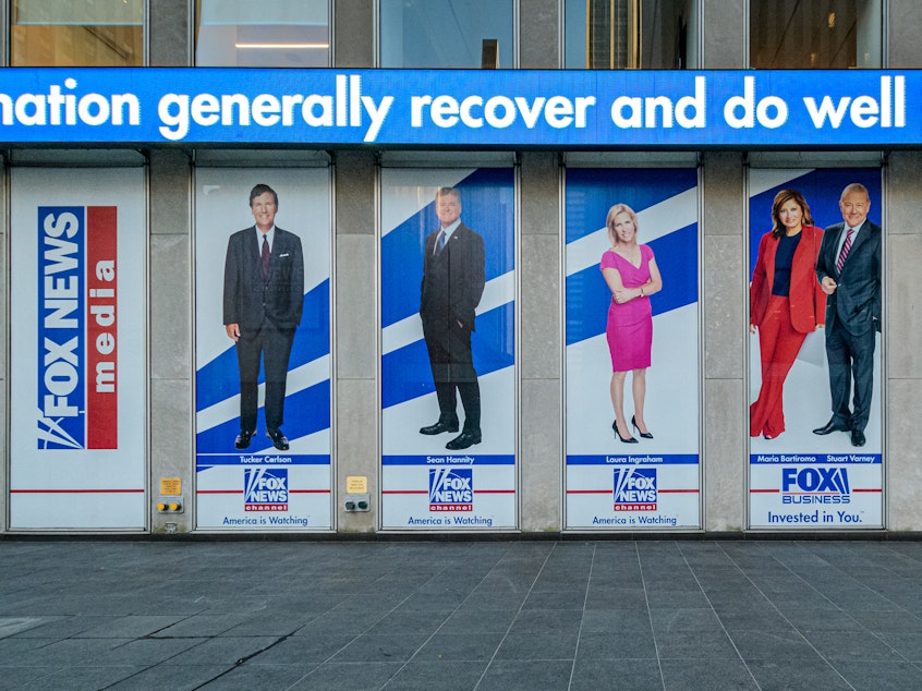caption: Among the stars being questioned under oath for Dominion Voting Systems' defamation suit against Fox News are Tucker Carlson, Sean Hannity and Maria Bartiromo. Banners bearing their images hang from Fox Corp headquarters in New York City, first, second and fourth from left, respectively.