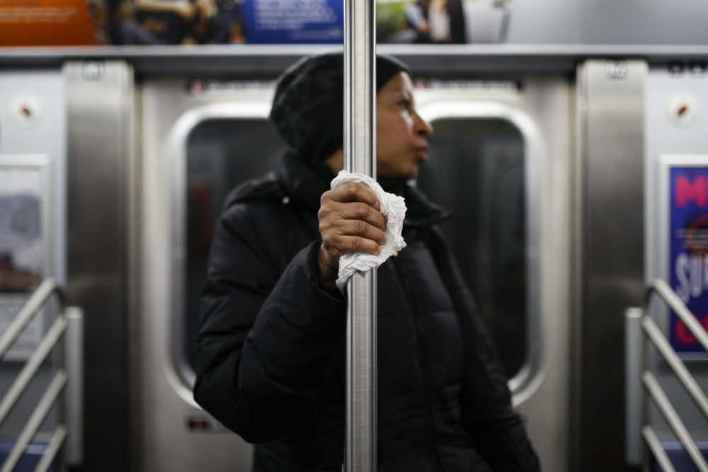 caption: A subway customer uses a tissue to protect her hand while holding onto a pole as COVID-19 concerns drive down ridership, Thursday, March 19, 2020, in New York. (John Minchillo/AP Photo)