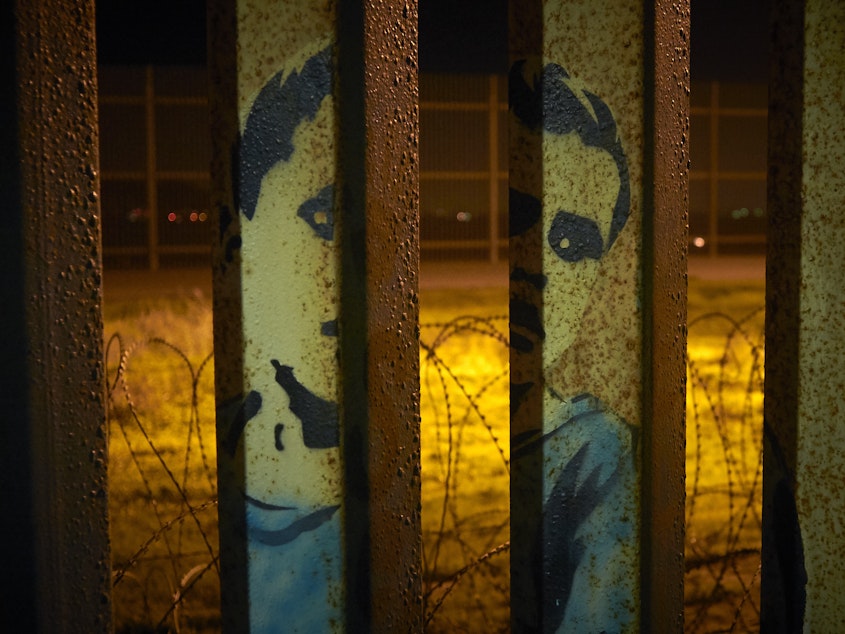 caption: An image of a boy is painted on the bars of the border wall, in front of coils of razor wire, seen from Tijuana, Mexico. President Trump's proposal to end the partial government shutdown includes funding for more border wall, but also provisions that further restrict asylum seekers.