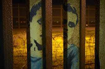 caption: An image of a boy is painted on the bars of the border wall, in front of coils of razor wire, seen from Tijuana, Mexico. President Trump's proposal to end the partial government shutdown includes funding for more border wall, but also provisions that further restrict asylum seekers.