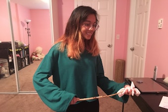 caption: Arya Barlinge uses her homemade wand, crafted from an apple tree, to demonstrate how she would channel energy to the headband she holds.