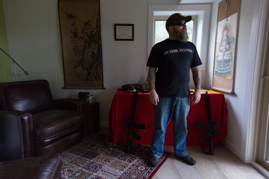 caption: Duke Aaron stands in front of his Buddhist alter and guns, in his Seattle home on February 15, 2020. Aaron said despite owning guns, he isn't voting on this one issue alone and places priority on health care issues. 
