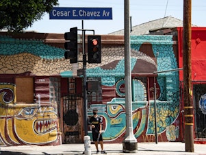 caption: A man waits to cross the street in the largely Latino neighborhood of East Los Angeles on Aug. 7. California has implemented a new health equity metric to help address the outsize effect of coronavirus on the state's communities of color.