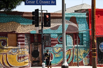 caption: A man waits to cross the street in the largely Latino neighborhood of East Los Angeles on Aug. 7. California has implemented a new health equity metric to help address the outsize effect of coronavirus on the state's communities of color.
