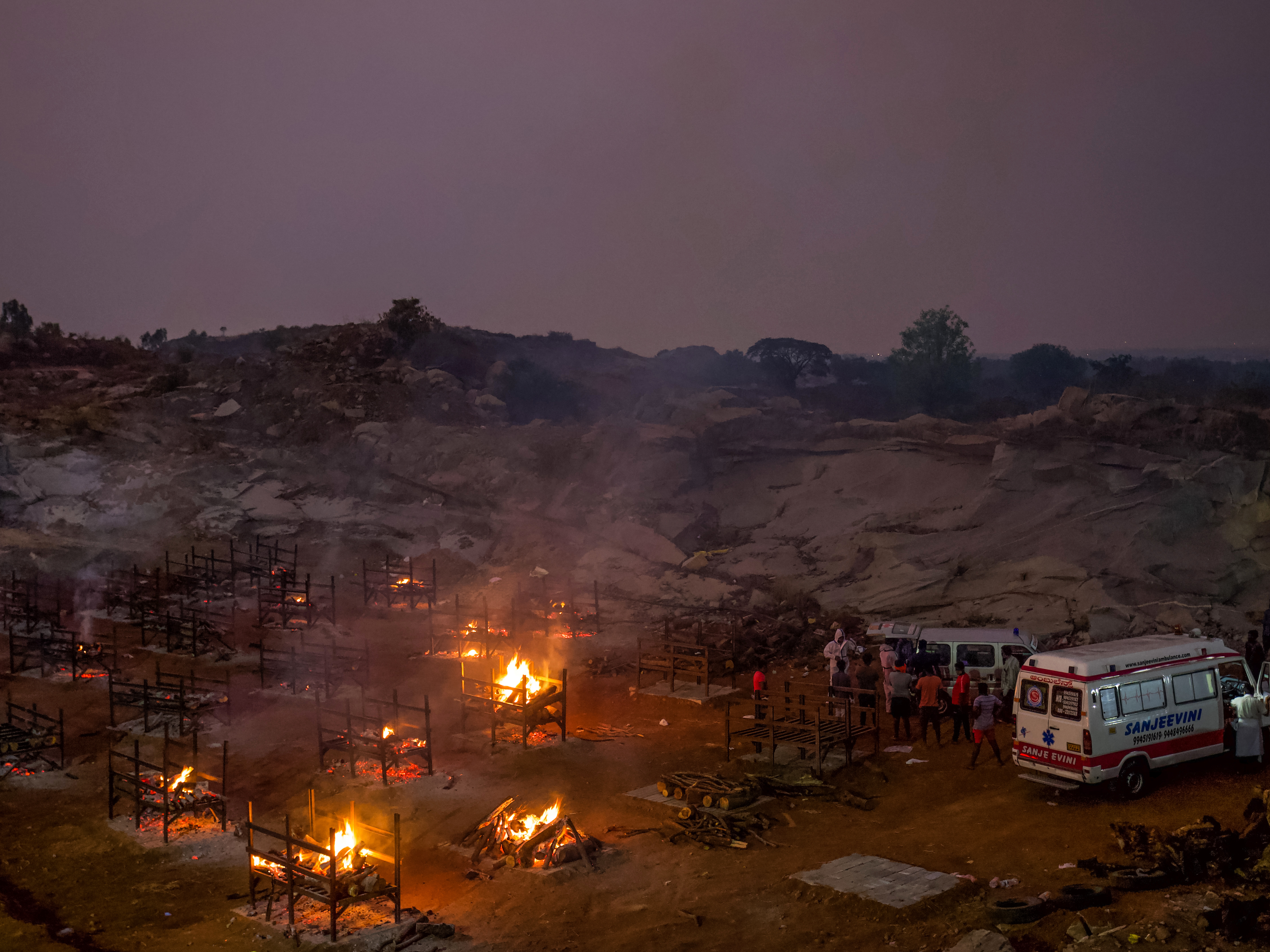 caption: Funeral pyres burn in a disused granite quarry repurposed to cremate the dead due to COVID-19 on Friday in Bengaluru, India. The U.S. is set to impose new travel restrictions against travelers from the country.