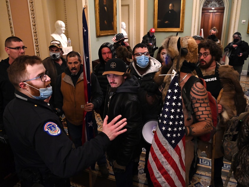 caption: Pro-Trump extremists, including Jacob Chansley, the "QAnon shaman" known for his painted face and horned hat, intended "to capture and assassinate elected officials," the Justice Department says in a new court filing. Chansley was taken into custody in Arizona.