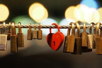 caption: a red heart shaped padlock amongst several other brass and copper ones on a rope