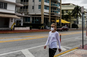 caption: A woman wearing a face mask walks on the deserted Ocean Drive amid the novel coronavirus pandemic in South Beach, Miami, on May 13. Pandemic war game simulation in the early 2000s foresaw an overwhelmed healthcare industry struggling to respond to unprecedented demand.