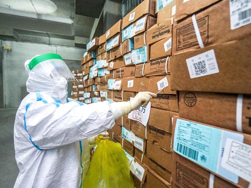caption: A health officer in a protective suit collects a sample from a package of imported frozen food for coronavirus rapid test at a wholesale market in China.