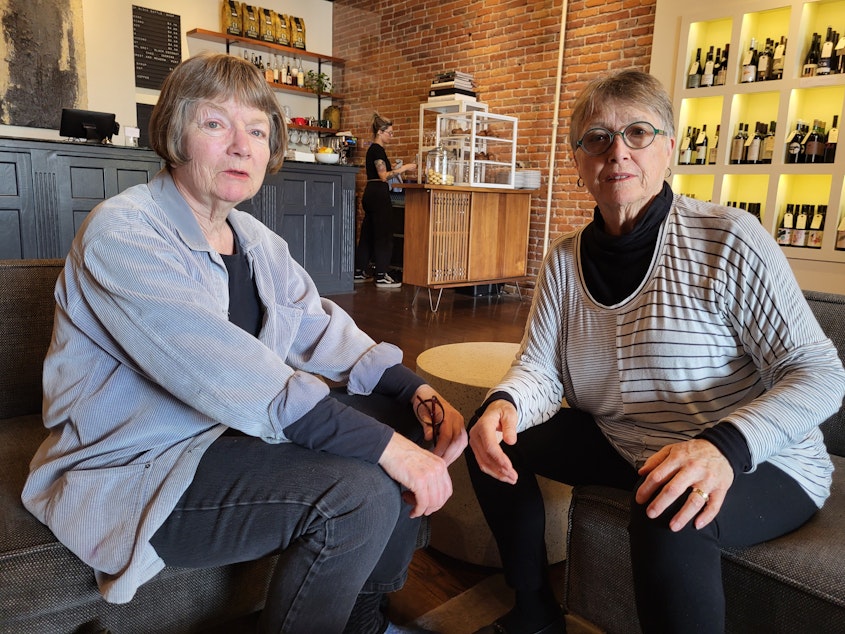 caption: Gina McMather and Debbi Steele sit in the Bishop Block Bottle Shop in Port Townsend in June 2024.